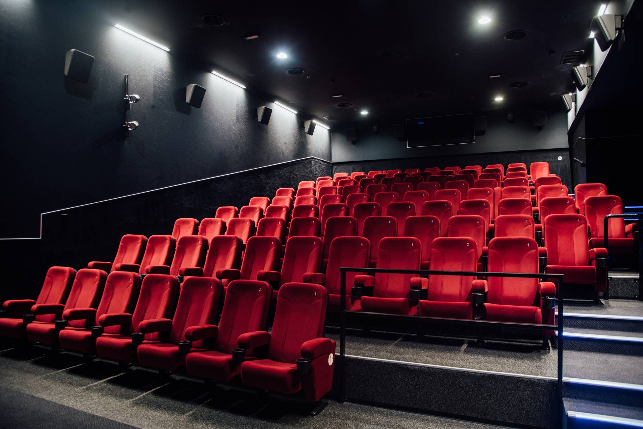 Киноафиша рядом со мной. Кинотеатр большой. Пустой кинотеатр с красными сиденьями. Красные кресла в кинотеатре. Ряд в кинотеатре пустой.