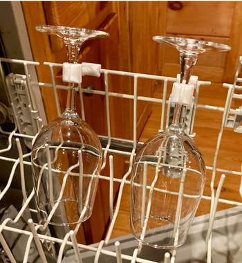 Two wine glasses upside-down in a dishwasher rack held by the white attachments 
