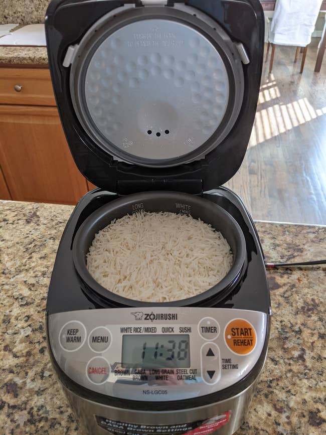 Rice cooker with a show  showing settings and a cookware  of uncooked atom   inside. Kitchen countertop successful  the background