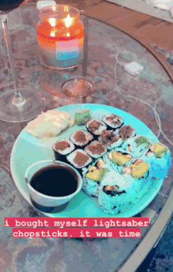 a gif of buzzfeed editor emma lord using the lightsaber chopsticks to eat sushi