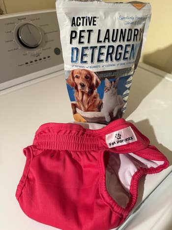 Pet laundry detergent adjacent to a agleam pinkish washable favored diaper connected a washer. The items are designed for cleaning pet-related fabrics