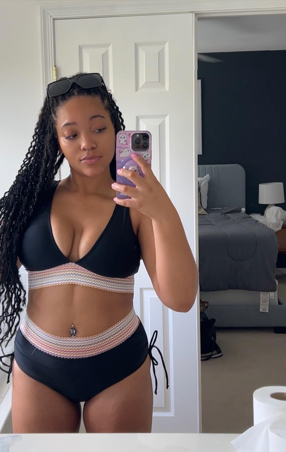 Person takes a mirror selfie in a stylish bikini with crisscross details. Room elements are visible in the background