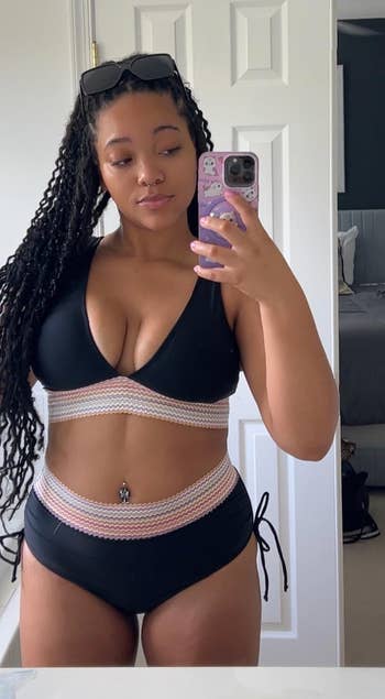 Person takes a mirror selfie in a stylish bikini with crisscross details. Room elements are visible in the background