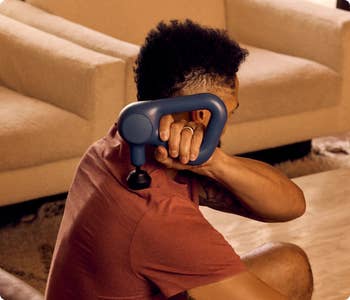 Person using a handheld massager on their shoulder in a home setting, demonstrating relaxation or self-care