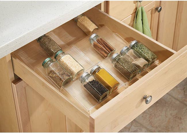 A transparent tiered drawer insert with spices resting on each of the three levels 