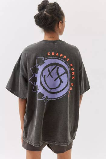 a model showing the back of an oversized dark gray t-shirt with the purple blink-182 logo on it