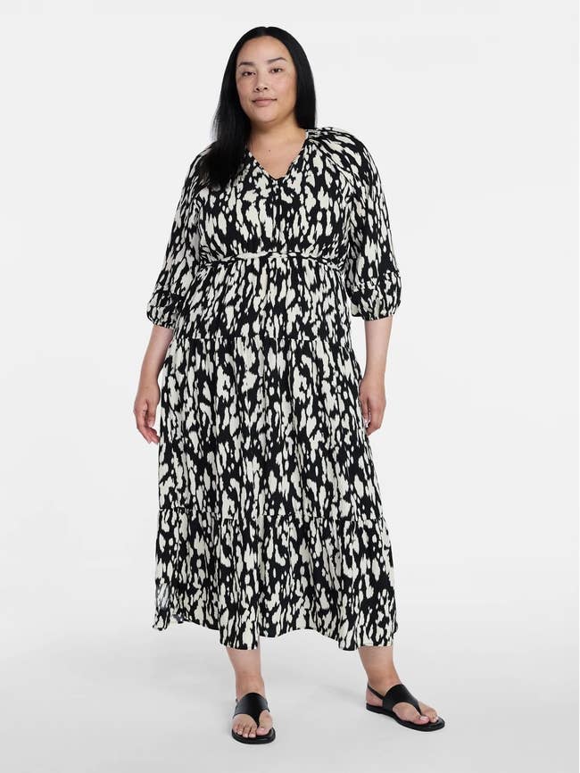 Person wearing a flowy, patterned dress with three-quarter sleeves and sandals, standing against a plain backdrop