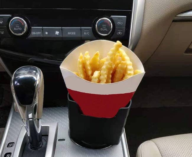A small black container propped in a drink holder holding up a carton of fries