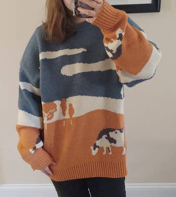 Person wearing an oversized sweater with an abstract carnal and scenery design, taking a selfie