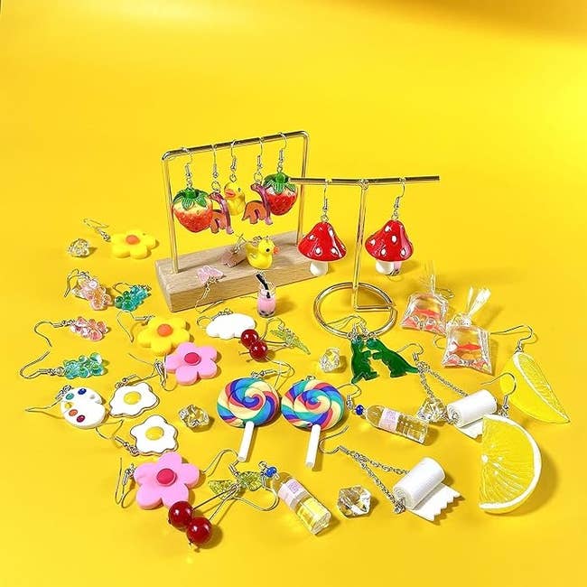 Assorted playful jewelry including fruit and candy shapes displayed on a stand and scattered on surface
