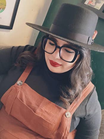 Person successful  a achromatic  chapeau  and glasses, wearing a stylish layered outfit with a turtleneck and overalls, looking down   thoughtfully