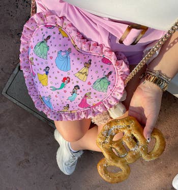 a buzzfeed writer wearing a pink heart-shaped pouch with frilled edges and a pattern of the disney princesses on it