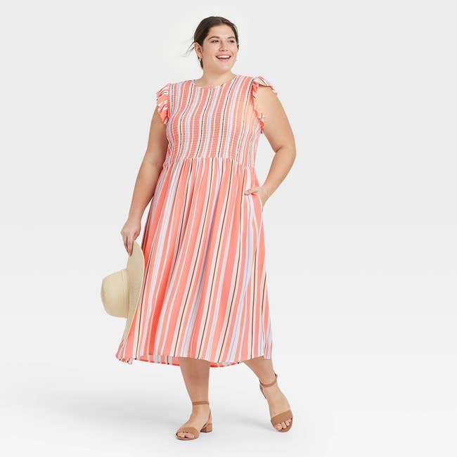model in the coral, white, brown, and lilac vertical stripe sleeveless dress with ruffle detail