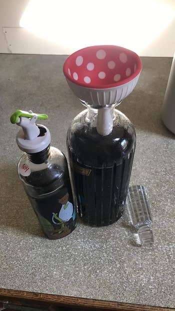 reviewer showing the mushroom funnel in a bottle refilling a soy sauce bottle