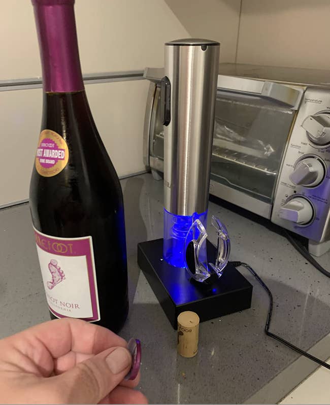 reviewer image of cylinder shaped blue lit opener on black base next to an uncorked wine bottle