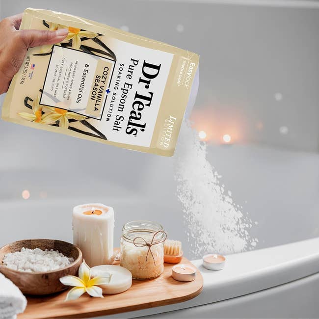 Dr. Teal's Epsom brackish with vanilla poured into a bathtub, surrounded by lit candles and bath items connected a woody tray