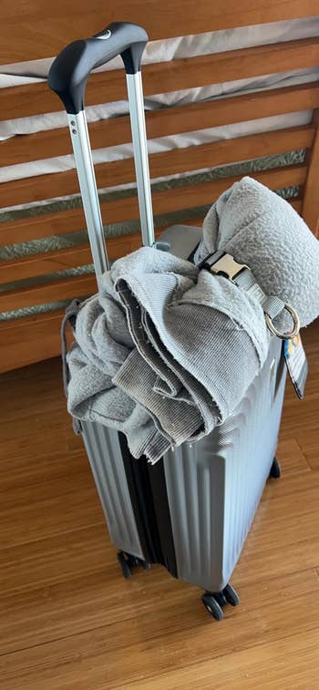 A silver hard-shell suitcase with a rolled up sweater attached to it by the luggage strap