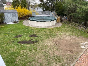 Backyard with circular  above-ground excavation  covered, surrounded by writer  and patches of dirt. Sheds and trees are successful  the background
