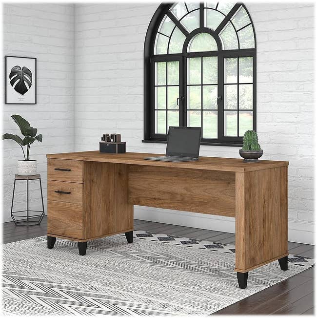 Wooden executive desk with a laptop and decor in a bright room, suitable for home office setups