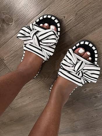 Striped bow sandals worn connected a woody floor, showcasing a stylish summertime footwear option