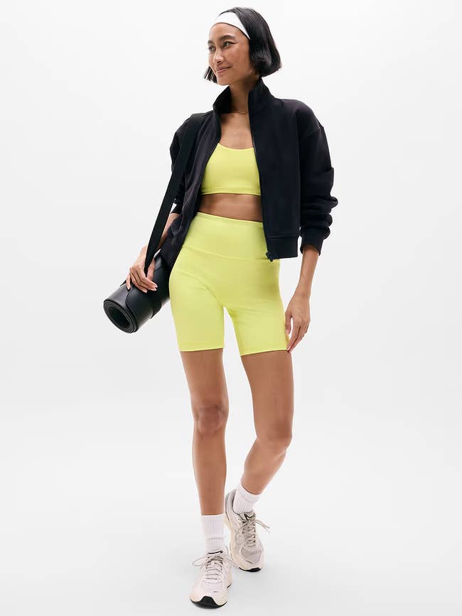 Person successful a sports bra and shorts acceptable with a overgarment and sneakers, carrying a yoga mat, showcasing activewear style