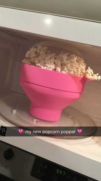 reviewer pic of the popper in pink in the microwave with popcorn coming out of it and the words 