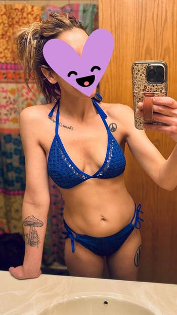 Person in a blue bikini taking a mirror selfie with a heart emoji covering the face