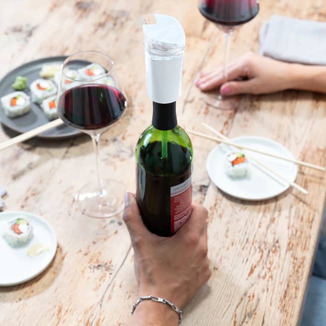 the white aerator and purifier on top of a wine bottle that's on a table filled with sushi and glasses of wine