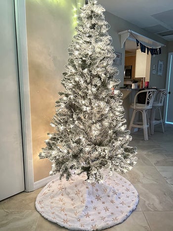 a reviewer's flocked tree with a white faux fur tree skirt under it with gold snowflakes on it