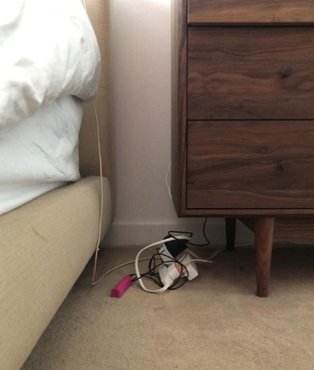 Reviewer pic of their cords next to their bed in a tangled mess