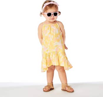 Toddler in a sleeveless dress and sandals, accessorized with sunglasses and a headband