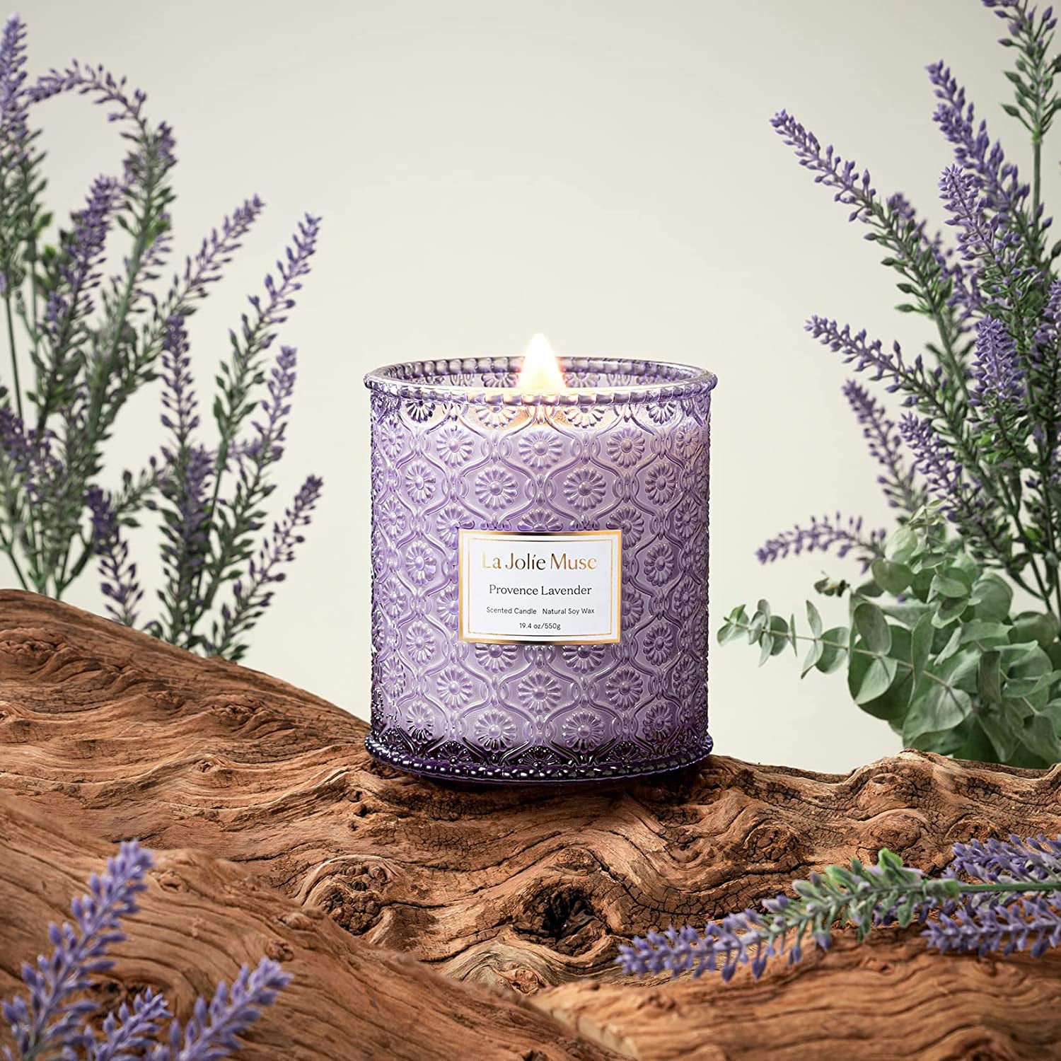 a lit lavender candle in a purple glass jar with lavender sprigs around it