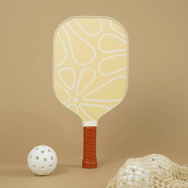 a yellow pickleball paddle with a white floral design on it