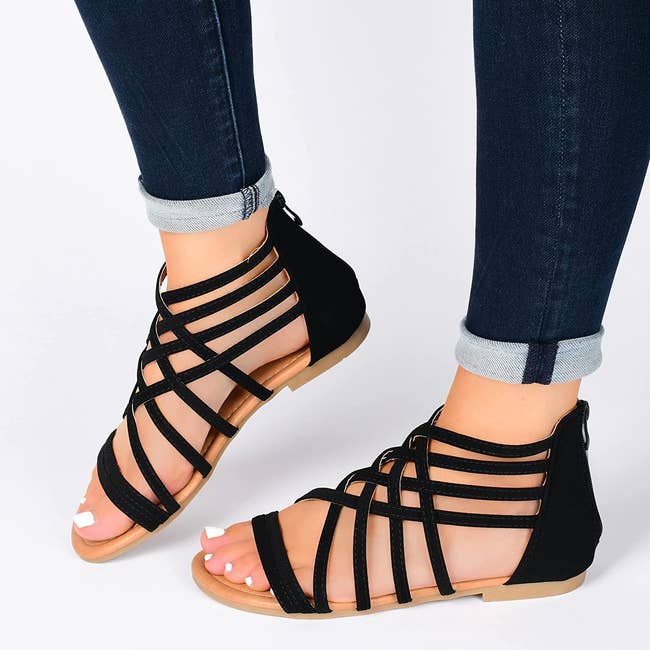 Model wearing black gladiator sandals with jeans on a white background