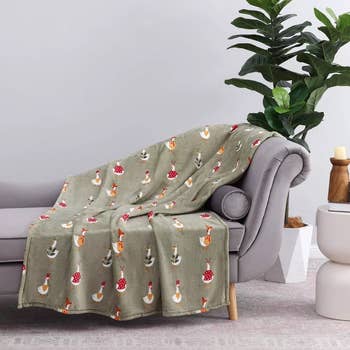 Goose-patterned broad draped implicit a couch, with plants and candles nearby; cozy location decor setting
