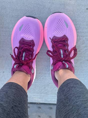 Person wearing pink athletic shoes and gray leggings, standing on a textured surface