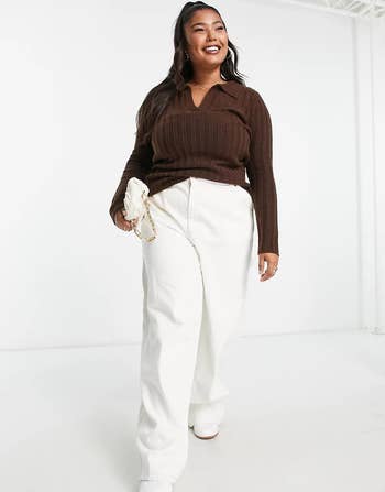 a zoomed-out shot of the same model wearing the sweater holding a white purse