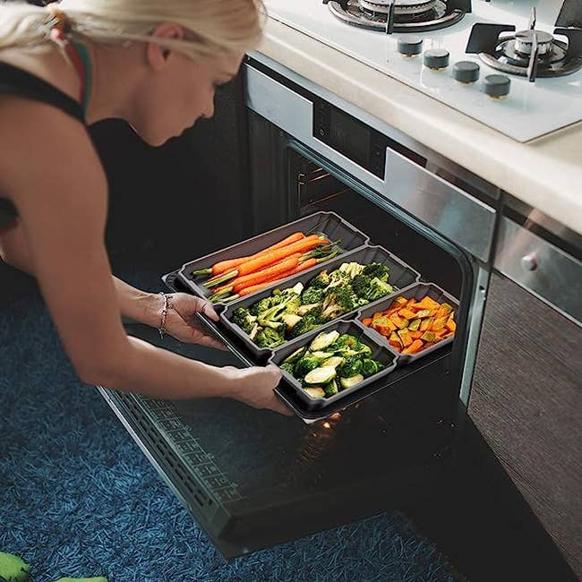 A model putting a baking sheet with silicone dividers filled with veggies in an oven