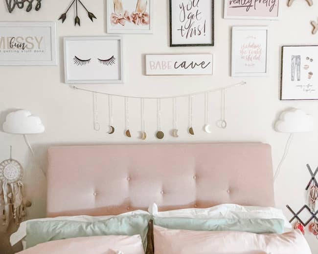 Wall decorated with inspirational quotes and art above a pink tufted headboard, suggesting cozy bedroom decor ideas for shopping