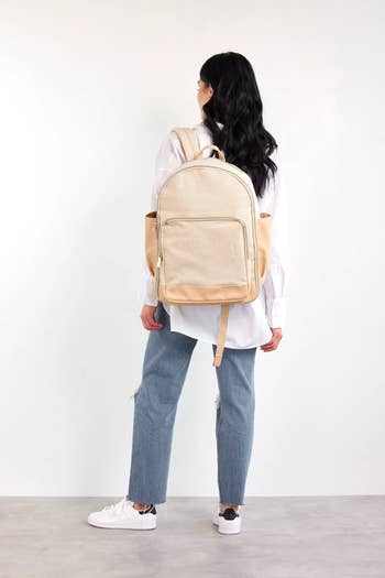 Model wearing off white backpack with front zippered pocket 