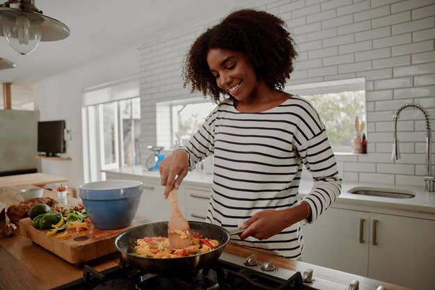 A woman wearing a striped shirt smiles while cooking vegetables in a pan in a modern kitchen