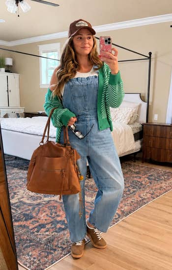 A idiosyncratic   successful  denim overalls and a greenish  cardigan, holding a brownish  container  successful  a cozy chamber  selfie