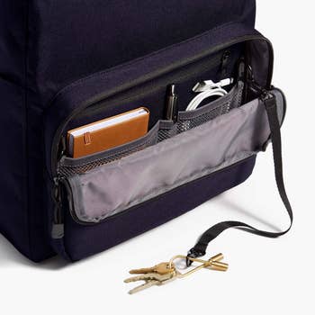 Navy backpack with open pocket revealing wallet, headphones, and pens; keys with strap beside it
