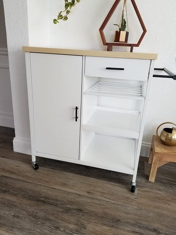 Reviewer image of white and light wooden microwave cart with drawer, cabinet door, and three shelves on a hardwood floor 