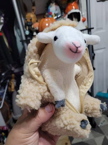 Hand holding a plush sheep with a backpack feature, ideal for a unique and cuddly storage option