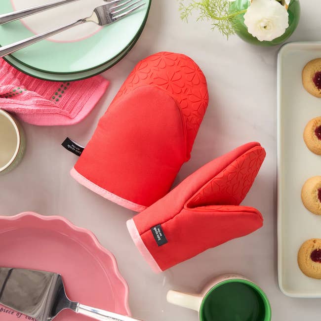Red oven mitts and kitchenware acceptable connected a array with pinkish dishes, greenish mug, cookies, and utensils. Perfect for baking and room use