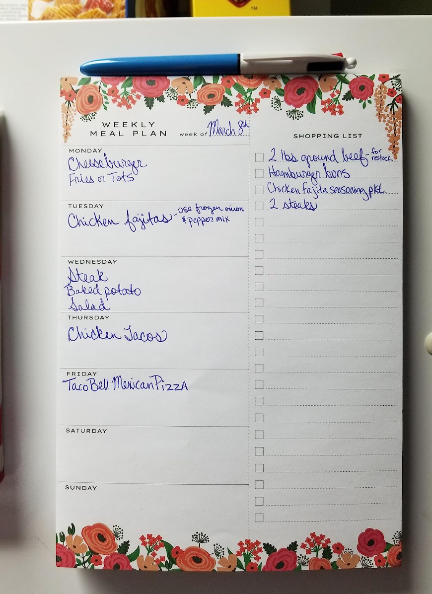 A white pad with orange floral detail that has space for meal prep for each day of the week on one side, and a blank grocery list on the other 