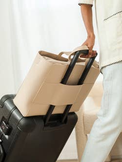 a beige tote bag strapped to a rolling suitcase handle 
