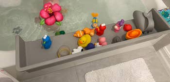 Bathtub with toy organizer holding various bath toys, including rubber ducks and sea creatures, beside a white bath mat