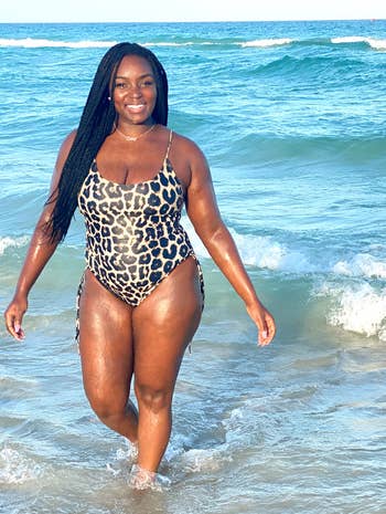 Person walking connected a beach, wearing a leopard people swimsuit, smiling and enjoying the waves